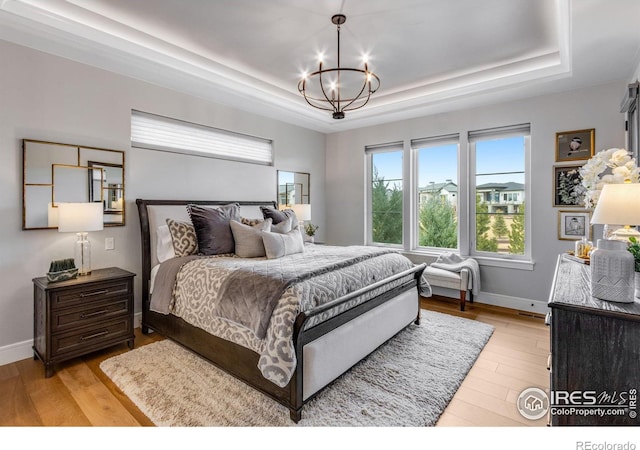 bedroom featuring light wood-style flooring, a chandelier, and a raised ceiling