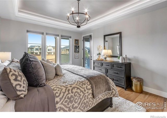 bedroom with a raised ceiling, light wood-style floors, access to outside, and an inviting chandelier