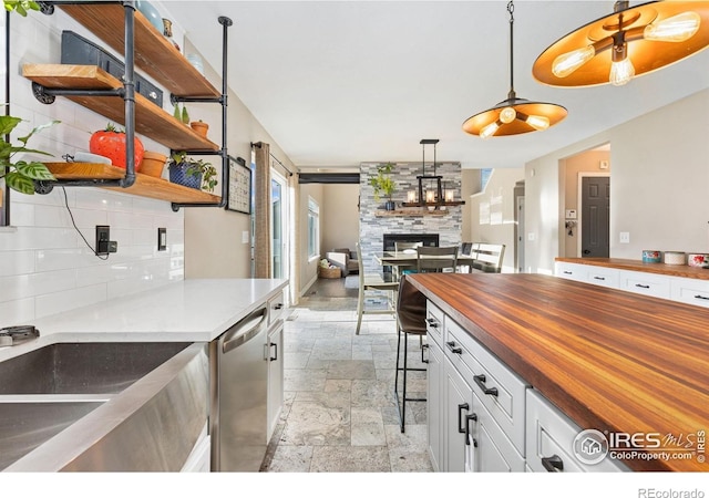 kitchen with stainless steel dishwasher, stone tile floors, white cabinetry, decorative backsplash, and butcher block counters