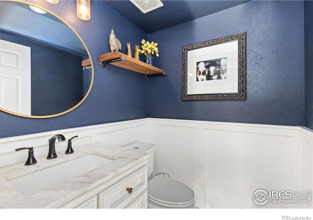 bathroom with a wainscoted wall, visible vents, vanity, and a decorative wall