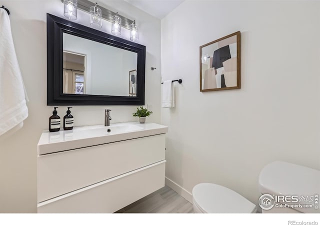 bathroom with wood finished floors, vanity, toilet, and baseboards