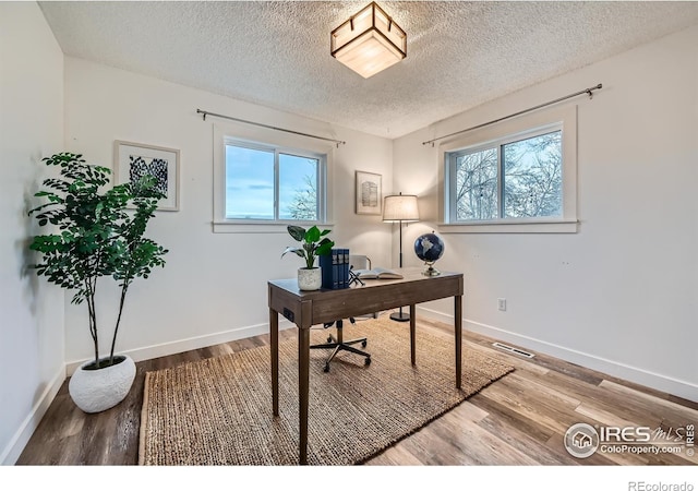 home office featuring plenty of natural light, baseboards, wood finished floors, and a textured ceiling