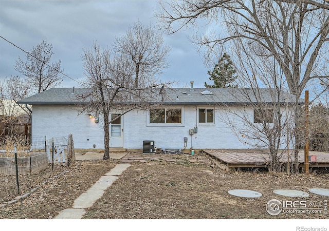 back of property with central air condition unit, a deck, fence, brick siding, and roof with shingles