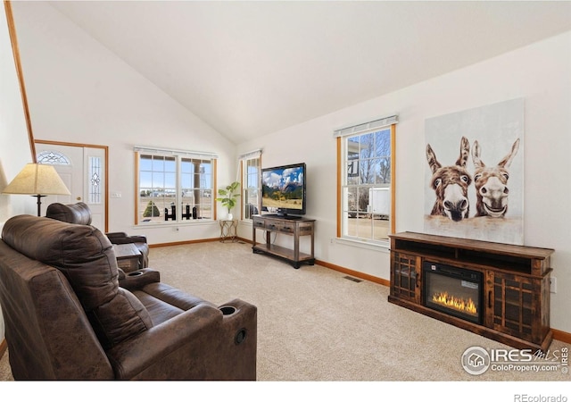 carpeted living area with high vaulted ceiling, baseboards, a glass covered fireplace, and visible vents