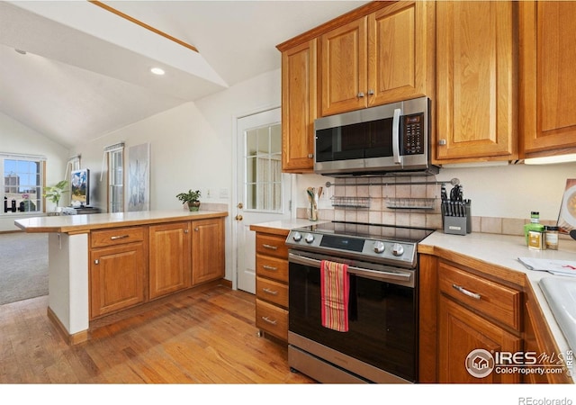 kitchen with light countertops, appliances with stainless steel finishes, light wood-style flooring, a peninsula, and lofted ceiling