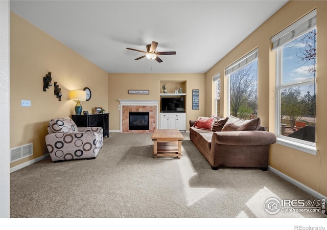 carpeted living room with visible vents, baseboards, ceiling fan, and a tile fireplace