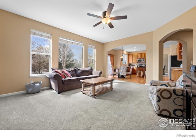 living area featuring a healthy amount of sunlight, arched walkways, and light colored carpet