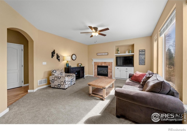 living room featuring ceiling fan, a tiled fireplace, built in features, carpet, and visible vents