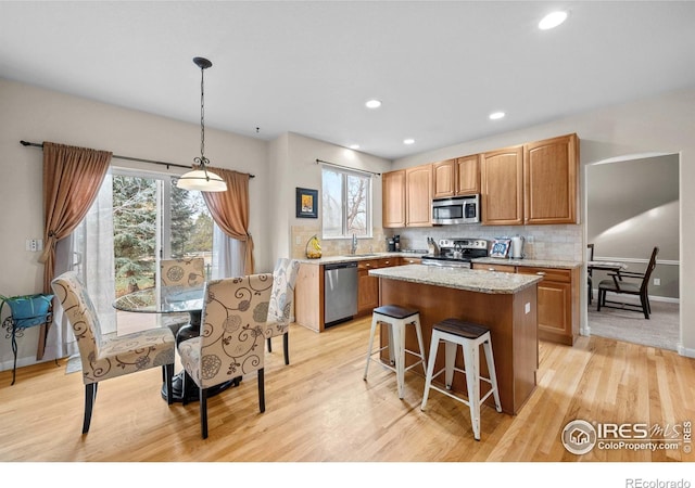 kitchen with stainless steel appliances, baseboards, decorative backsplash, light wood-type flooring, and a kitchen island