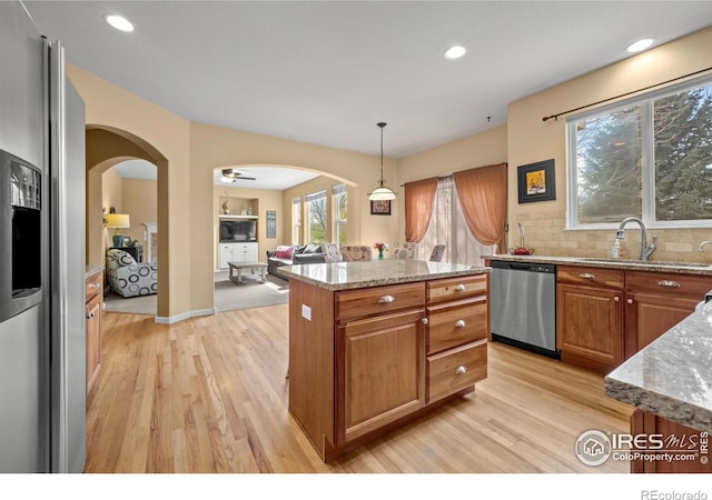 kitchen with arched walkways, light stone countertops, appliances with stainless steel finishes, and light wood-type flooring