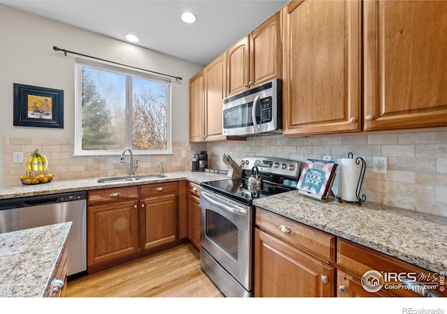 kitchen featuring decorative backsplash, appliances with stainless steel finishes, a sink, light stone counters, and light wood finished floors