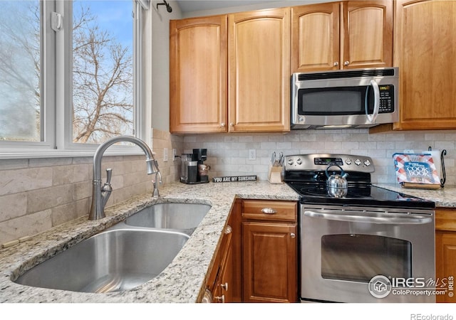 kitchen featuring stainless steel appliances, light stone counters, a sink, and tasteful backsplash