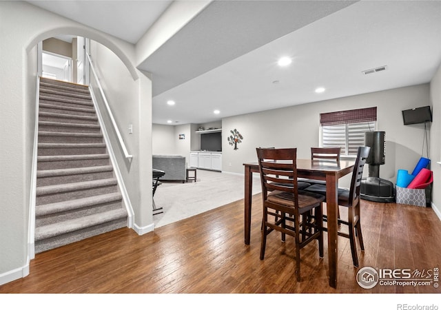 dining space featuring wood-type flooring, baseboards, visible vents, and stairway