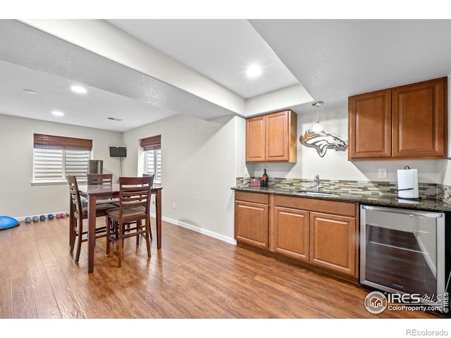 kitchen with brown cabinetry, wood finished floors, beverage cooler, baseboards, and a sink