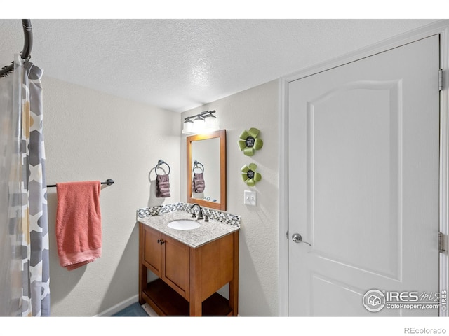 full bath with a textured ceiling, a textured wall, and vanity