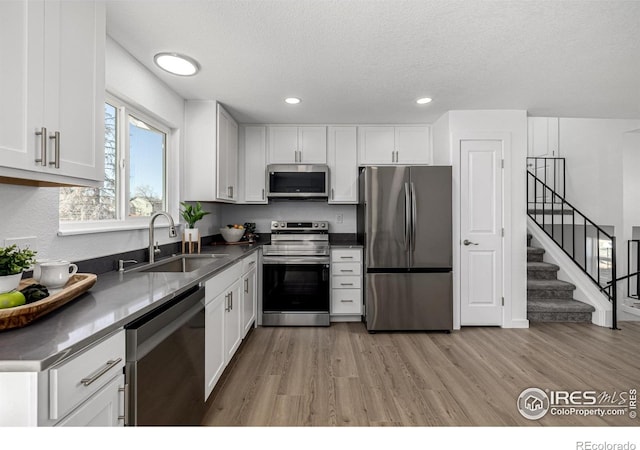 4752 E 108th Pl, Thornton, CO 80233 - kitchen with white cabinets, stainless steel appliances, light wood-style flooring, a sink, and a textured ceiling