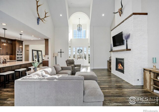 living area featuring dark wood finished floors, high vaulted ceiling, a stone fireplace, recessed lighting, and arched walkways