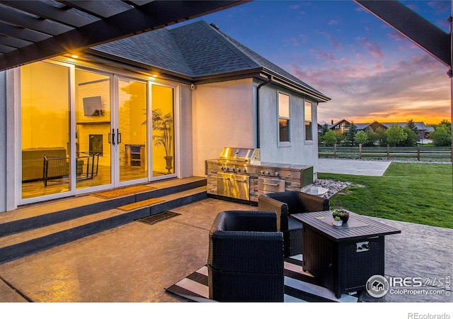 patio terrace at dusk featuring exterior kitchen, a pergola, and a grill