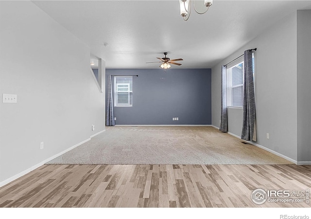unfurnished room with light wood finished floors, baseboards, and ceiling fan with notable chandelier