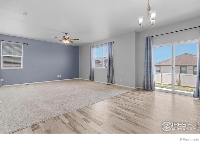 unfurnished room featuring wood finished floors, baseboards, and ceiling fan with notable chandelier