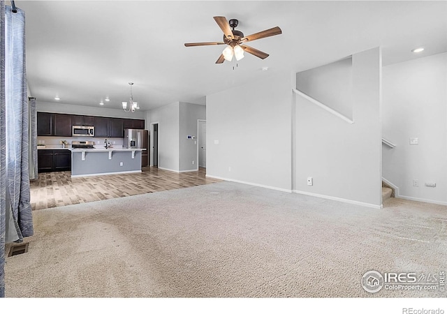 unfurnished living room with stairs, ceiling fan with notable chandelier, light carpet, baseboards, and recessed lighting