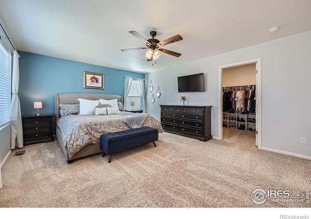 carpeted bedroom featuring a walk in closet, a closet, baseboards, and ceiling fan