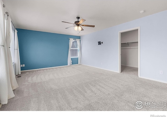 unfurnished bedroom with a walk in closet, carpet flooring, baseboards, and ceiling fan