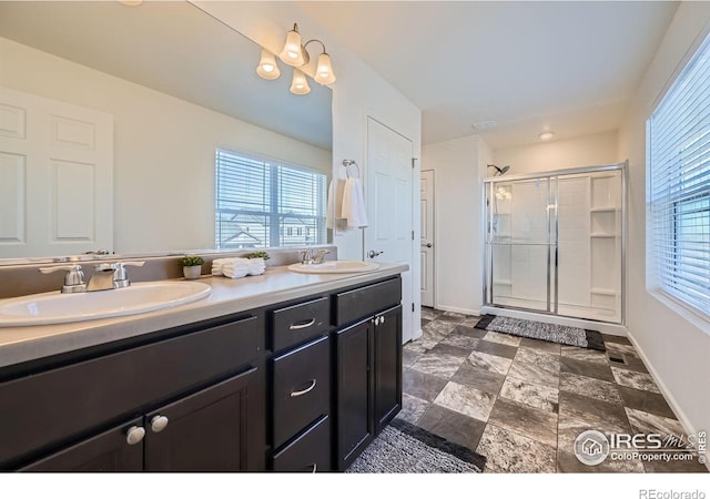 bathroom featuring baseboards, double vanity, a stall shower, and a sink