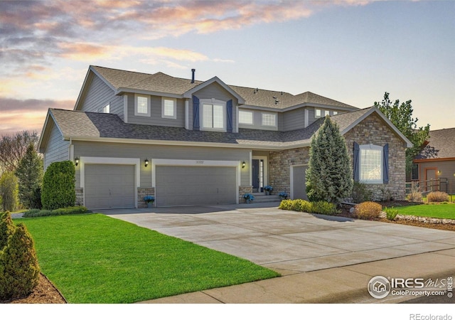 traditional home with concrete driveway, an attached garage, a yard, and stone siding