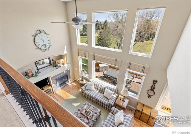 living area featuring a tile fireplace, a healthy amount of sunlight, a towering ceiling, and a ceiling fan