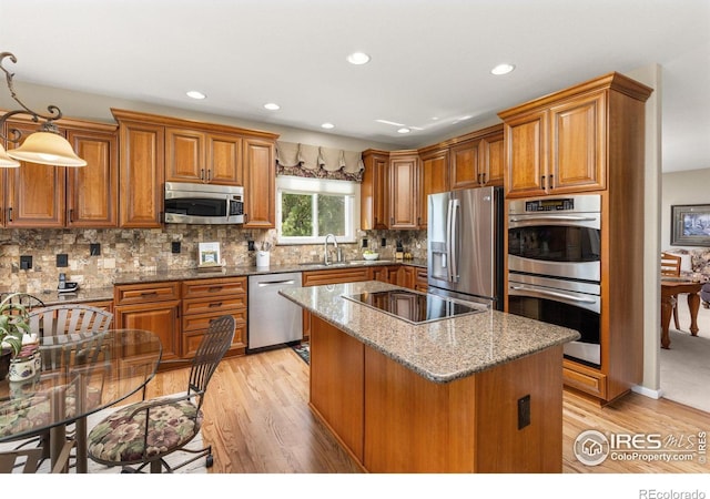 kitchen featuring a center island, brown cabinetry, light wood-style floors, stainless steel appliances, and stone counters