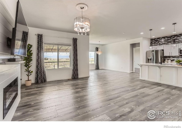 6021 Sandstone Cir, Erie, CO 80516 - unfurnished living room with recessed lighting, light wood-style floors, a glass covered fireplace, and a notable chandelier
