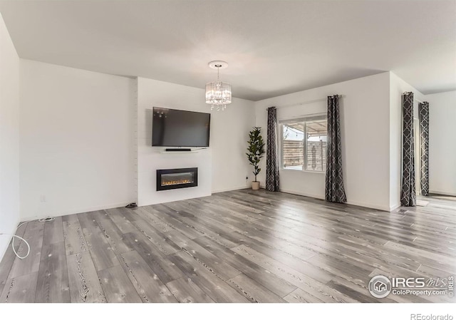 6021 Sandstone Cir, Erie, CO 80516 - unfurnished living room with a glass covered fireplace, wood finished floors, and a notable chandelier