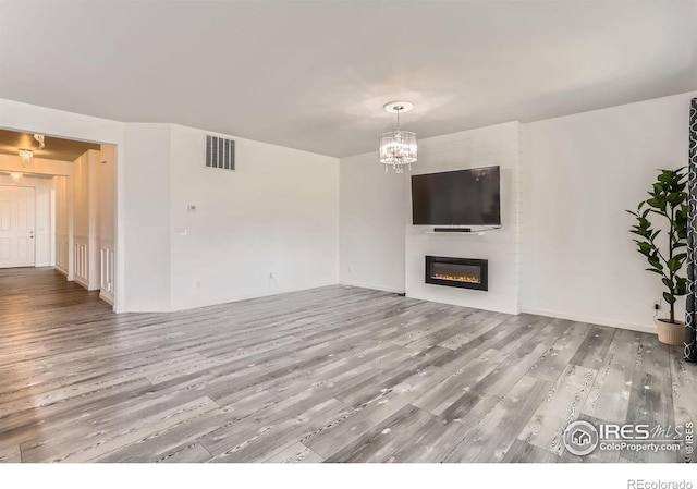 6021 Sandstone Cir, Erie, CO 80516 - unfurnished living room featuring an inviting chandelier, a glass covered fireplace, wood finished floors, and visible vents