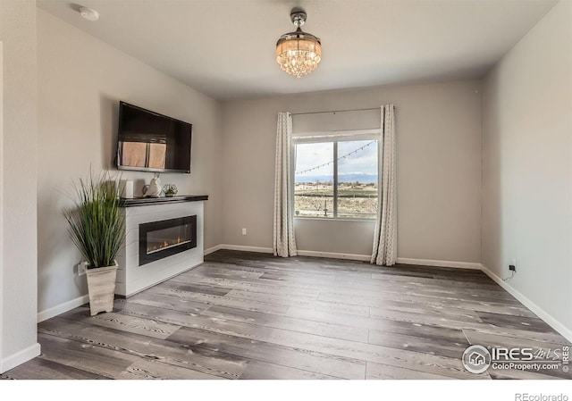 6021 Sandstone Cir, Erie, CO 80516 - unfurnished living room with baseboards, wood finished floors, a glass covered fireplace, and an inviting chandelier