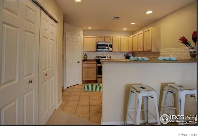 kitchen featuring light tile patterned flooring, a kitchen bar, recessed lighting, backsplash, and stainless steel appliances