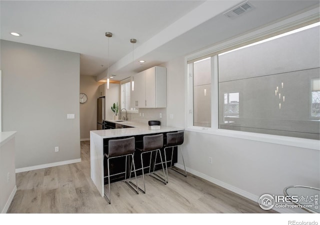 kitchen with a kitchen breakfast bar, visible vents, a sink, light wood-type flooring, and white cabinetry