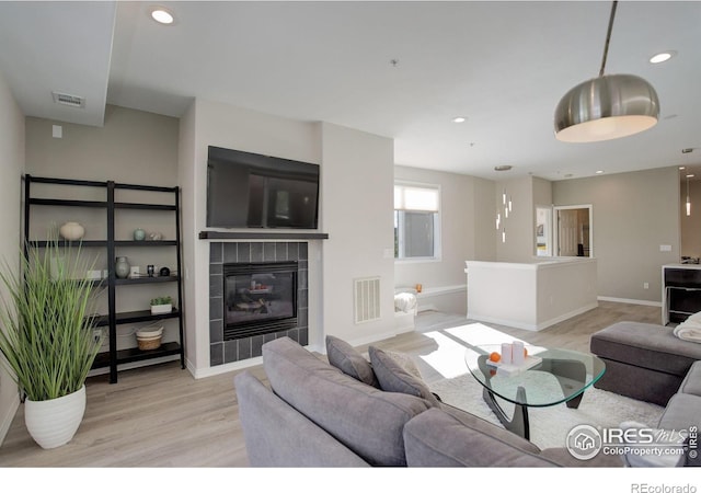 living room featuring light wood finished floors, baseboards, a tiled fireplace, and visible vents