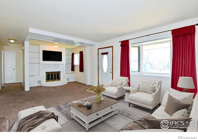 carpeted living area with a fireplace, a textured ceiling, visible vents, and plenty of natural light