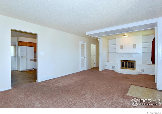 unfurnished living room featuring a textured ceiling, carpet, a fireplace, baseboards, and visible vents