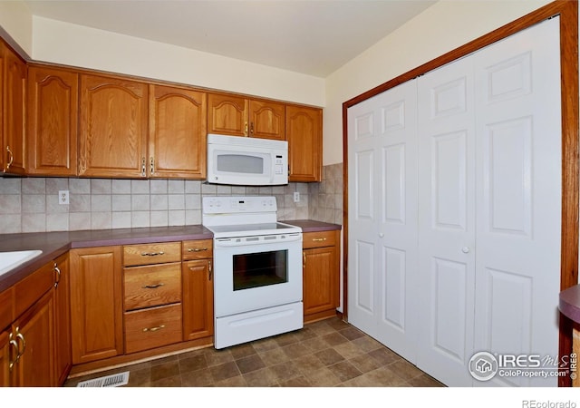 kitchen with brown cabinetry, white appliances, dark countertops, and tasteful backsplash