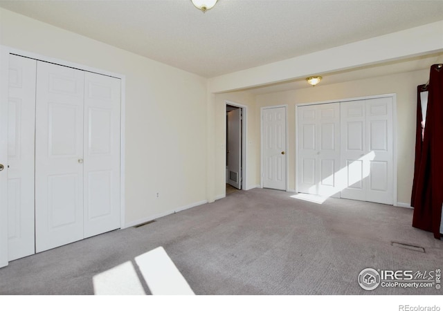 unfurnished bedroom featuring visible vents, carpet flooring, baseboards, and multiple closets