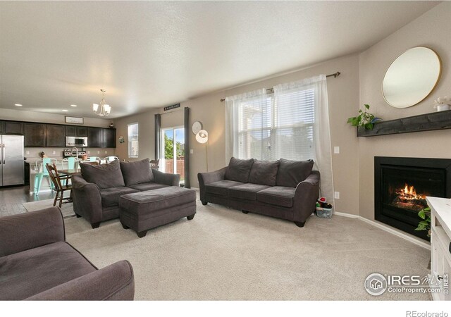 living room with an inviting chandelier, light colored carpet, baseboards, a glass covered fireplace, and recessed lighting