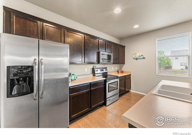 6747 Grainery Rd, Timnath, CO 80547 - kitchen featuring appliances with stainless steel finishes, light wood-style floors, dark brown cabinetry, recessed lighting, and light countertops