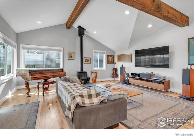 living area with a wood stove, light wood-style flooring, recessed lighting, baseboards, and vaulted ceiling with beams