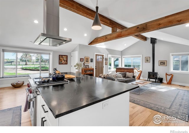 kitchen featuring island range hood, a wood stove, stainless steel stove, open floor plan, and vaulted ceiling with beams