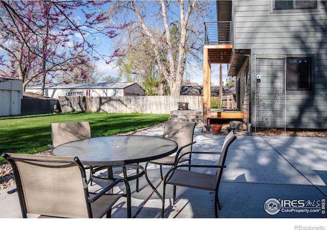 view of patio featuring fence, outdoor dining space, a storage shed, a balcony, and an outdoor structure