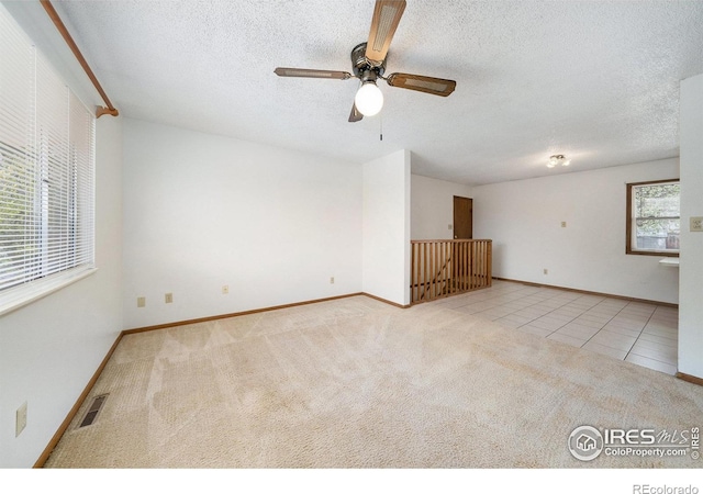 tiled empty room with a textured ceiling, baseboards, visible vents, carpet, and a ceiling fan