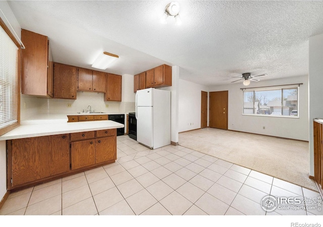 kitchen with light carpet, a sink, freestanding refrigerator, brown cabinetry, and light countertops