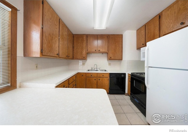 kitchen with a sink, tasteful backsplash, brown cabinets, light countertops, and black appliances